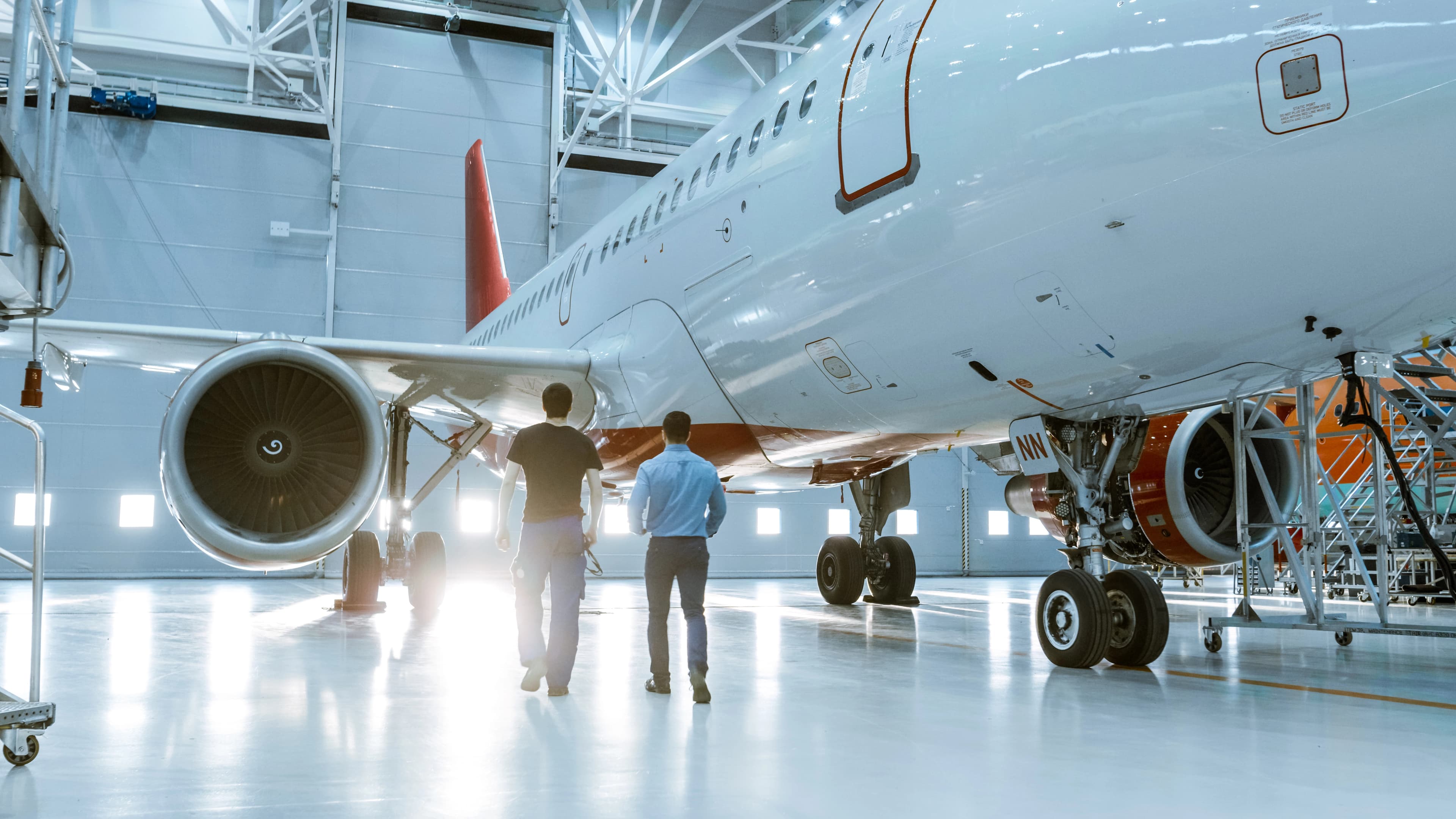 Zwei Techniker gehen in einem hellen Hangar auf ein großes Passagierflugzeug zu.